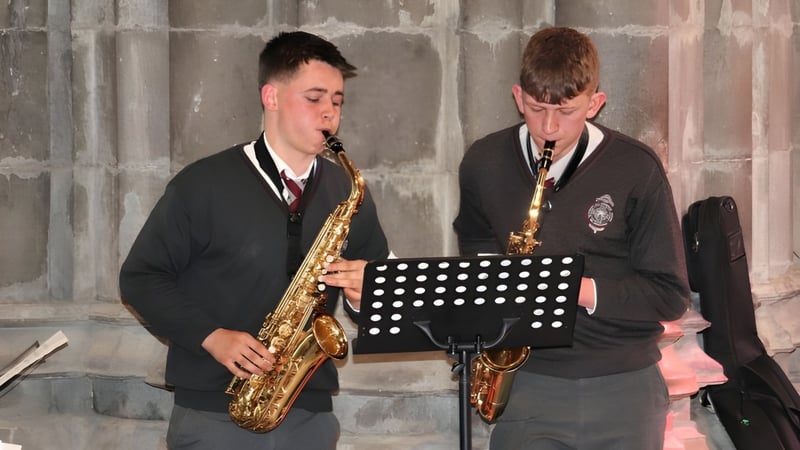 Zwei Schüler der Christian Brothers School Kilkenny spielen Saxophone auf einer Bühne vor einer Steinwand.