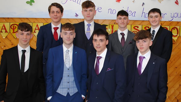 Eine Gruppe Schüler der Christian Brothers School Kilkenny steht in formeller Kleidung vor einer bunten Klassenzimmerkulisse.