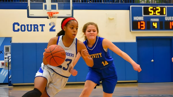 Zwei Schülerinnen der Christian Central Academy konkurrieren auf dem Basketballfeld um den Ball vor einer Anzeigetafel.