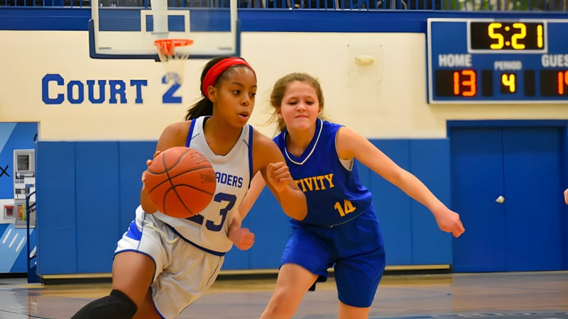 Zwei Schülerinnen der Christian Central Academy konkurrieren auf dem Basketballfeld um den Ball vor einer Anzeigetafel.