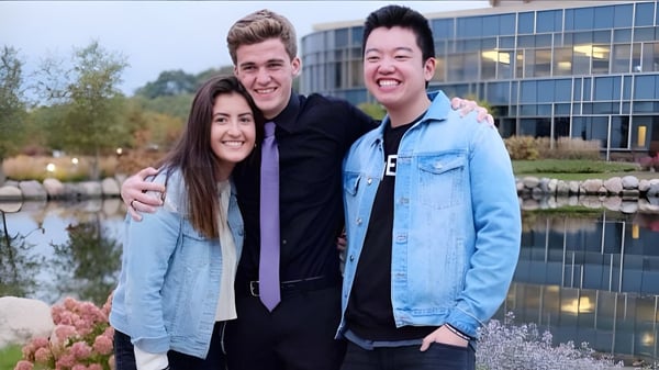 Drei Schülerinnen und Schüler der Christian Life School stehen vor einem modernen Gebäude mit Wasserspiegelung.