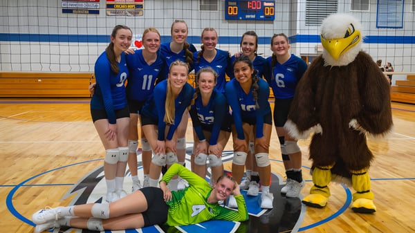 Eine Gruppe weiblicher Volleyballspielerinnen in blauen Trikots posiert zusammen auf dem Basketballfeld der Christian Life School mit einem gelben Maskottchen.