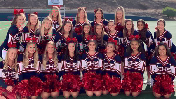 Eine Gruppe von Cheerleadern posiert mit einheitlichen Uniformen und Pompons auf dem Sportfeld der Christian Unified Schools.