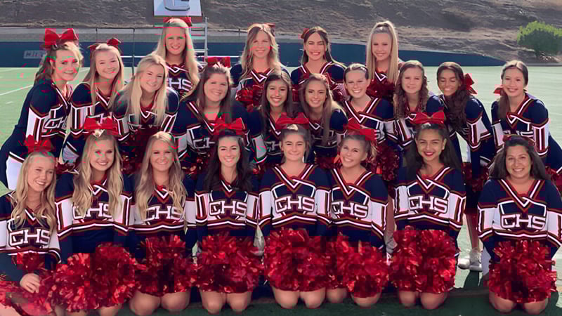 Eine Gruppe von Cheerleadern posiert mit einheitlichen Uniformen und Pompons auf dem Sportfeld der Christian Unified Schools.