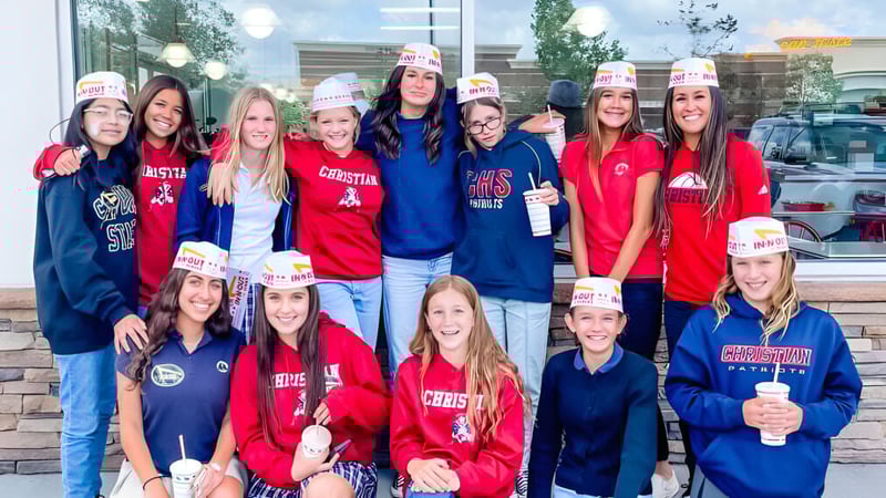 Eine Gruppe Schülerinnen der Christian Unified Schools trägt einheitliche Sporttrikots und Mützen vor einem Schulgebäude.