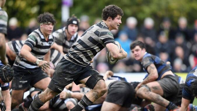 Schüler von Christ's College spielen in einem Rugby-Scrum auf dem grasbewachsenen Spielfeld mit Zuschauern im Hintergrund.