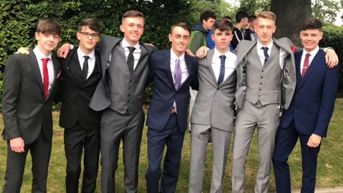 Eine Gruppe von Schülern in formeller Kleidung steht draußen auf dem Campus des Christ's College vor Bäumen.