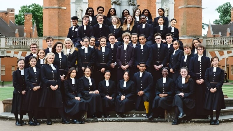 Eine Gruppe Schüler in formeller akademischer Kleidung steht vor dem historischen Backsteingebäude der Christ's Hospital School.