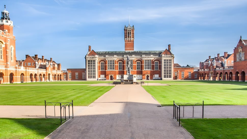 Das historische Backsteingebäude mit hohem Turm auf dem Campus der Christ's Hospital School ist von grünem Rasen und einem gepflasterten Weg umgeben.