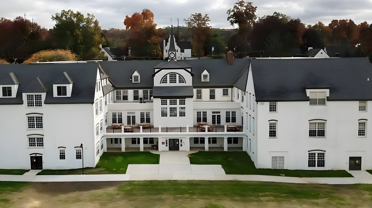 Das große weiße Gebäude der Church Farm School mit zentralem Turm und Bogenfenstern umgeben von bunten Bäumen.