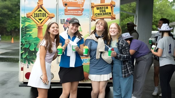 Eine Gruppe Schüler der Cincinnati Christian Schools steht vor einem bunten Karnevals-Hintergrund mit Schildern und Dekorationen.