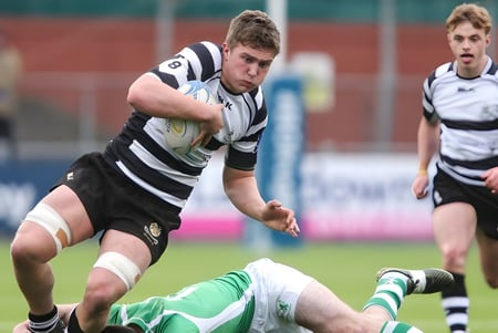 Ein Rugbyspieler der Cistercian College läuft mit dem Ball über das Spielfeld während ein anderer Spieler am Boden liegt.