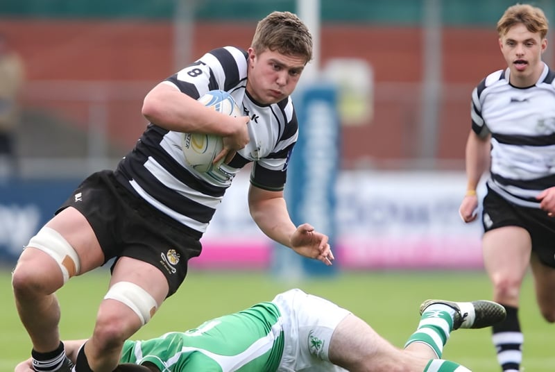 Ein Rugbyspieler der Cistercian College läuft mit dem Ball über das Spielfeld während ein anderer Spieler am Boden liegt.