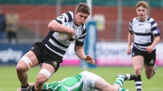 Ein Rugbyspieler der Cistercian College tackelt einen Gegner im grünen Trikot auf dem Sportfeld.