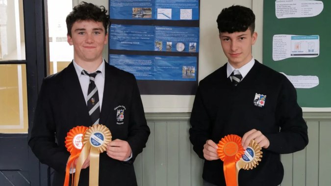 Zwei Schüler im Schuluniform stehen in einem Klassenraum des Cistercian College und halten orangefarbene Schleifen.