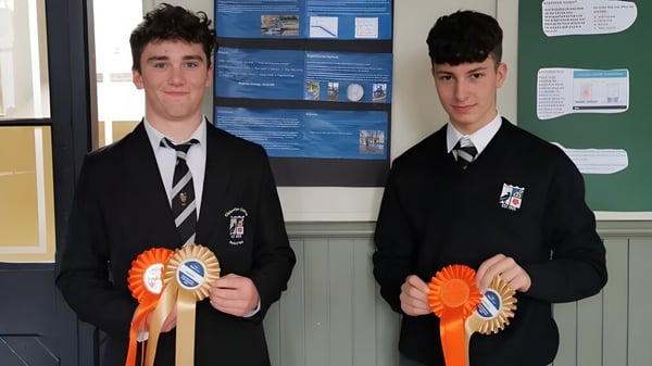 Zwei Schüler in Schuluniformen halten orangefarbene Bänder vor einem Informationsbrett auf dem Campus des Cistercian College.