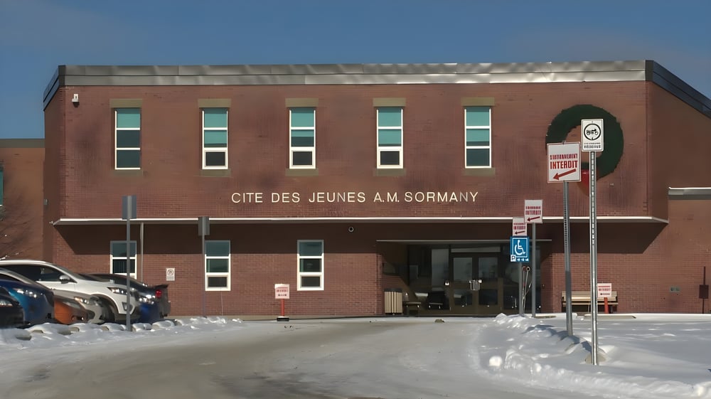 Das Backsteingebäude der Cité des Jeunes A.-M.-Sormany mit großen Fenstern an einer schneebedeckten Straße.