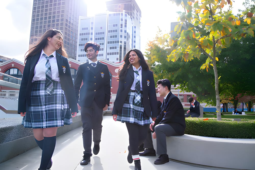 Eine Gruppe Schülerinnen und Schüler der City Vancouver Academy High School geht gemeinsam auf dem Schulcampus mit hohen Gebäuden und Bäumen.