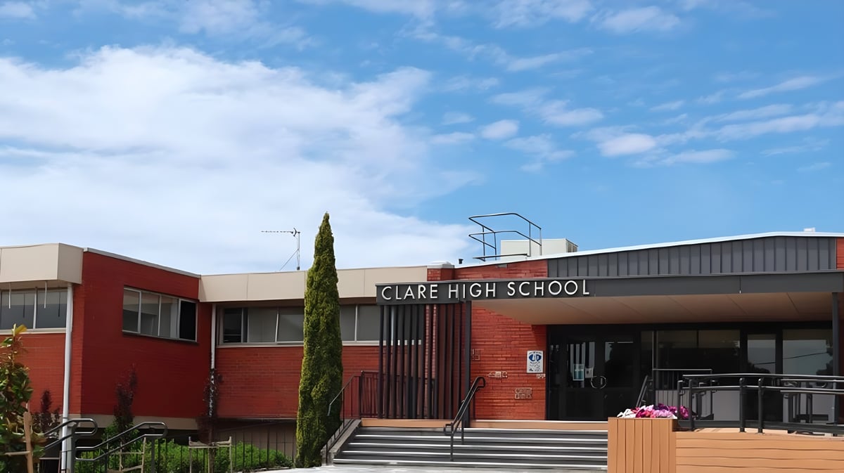Das rote Backsteingebäude der Clare High School ist von Bäumen umgeben und steht unter einem bewölkten blauen Himmel.
