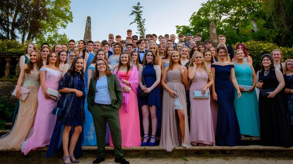Eine Gruppe junger Frauen in eleganten Kleidern steht gemeinsam vor einer landschaftlichen Kulisse auf dem Campus der Claremont School.