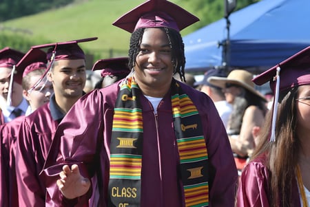 Absolventen in violetten Talaren der Claremont Secondary School stehen vor einem blauen Zelt und Bäumen.