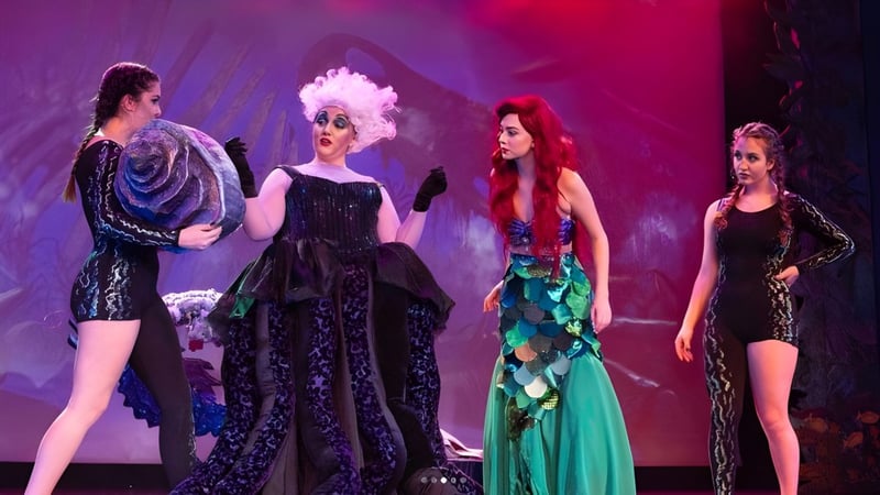 Vier Schülerinnen und Schüler der Claremont Secondary School tragen bunte Kostüme auf einer Bühne mit lebhaftem Theaterhintergrund.