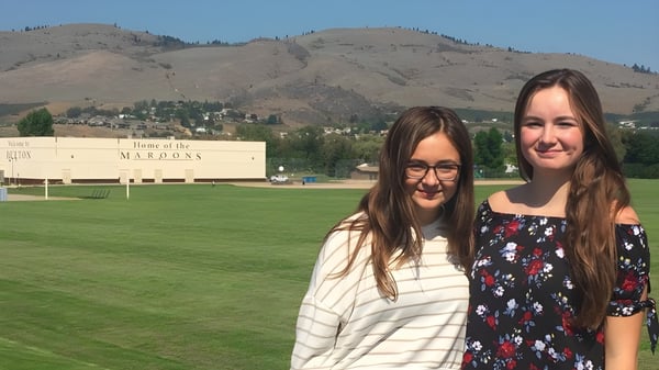 Zwei Schülerinnen stehen auf einem grasbewachsenen Feld mit Blick auf die Berge auf dem Gelände der Clarence Fulton Secondary School.