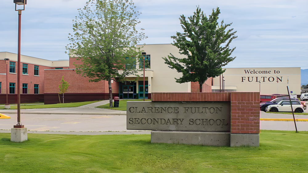 Backstein-Schild mit der Aufschrift Clarence Fulton Secondary School vor dem Schulgebäude und Bäumen.