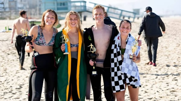 Eine Gruppe von Schülerinnen und Schülern der Clarence High School steht am Strand mit einer Stadtkulisse im Hintergrund.