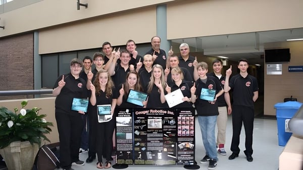 Eine Gruppe Schüler steht vor dem Gebäude der Clarenville High School und hält verschiedene Gegenstände sowie ein Schild.