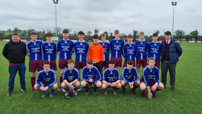 Eine Gruppe männlicher Schüler des Clarin College posiert in blauen Fußballtrikots auf einem Rasenfeld mit bewölktem Himmel.