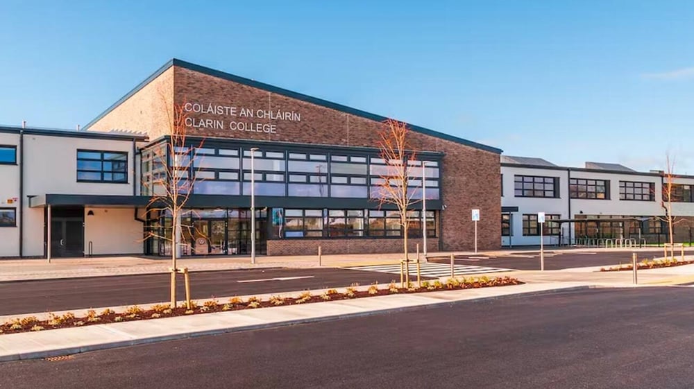 Das moderne Backsteingebäude des Clarin College mit großen Fenstern und einem gut sichtbaren Schild ist von einem gepflasterten Bereich mit Blumenbeeten umgeben.