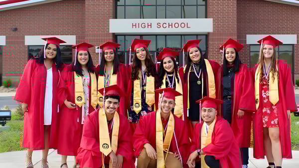 Eine Gruppe von Absolventinnen und Absolventen der Clarksville High School steht in roten Talaren vor dem Schulgebäude und feiert ihren Abschluss.