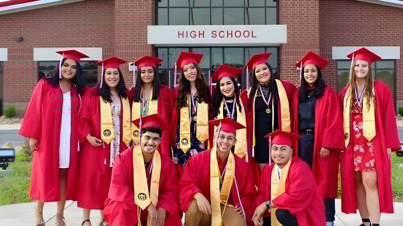 Eine Gruppe von Absolventinnen und Absolventen der Clarksville High School steht in roten Talaren vor dem Schulgebäude und feiert ihren Abschluss.