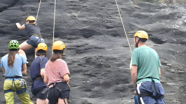 Schüler des Classic Plus Programms tragen Schutzhelme und stehen mit Gurten auf felsigem Gelände bei einer Outdoor-Aktivität.
