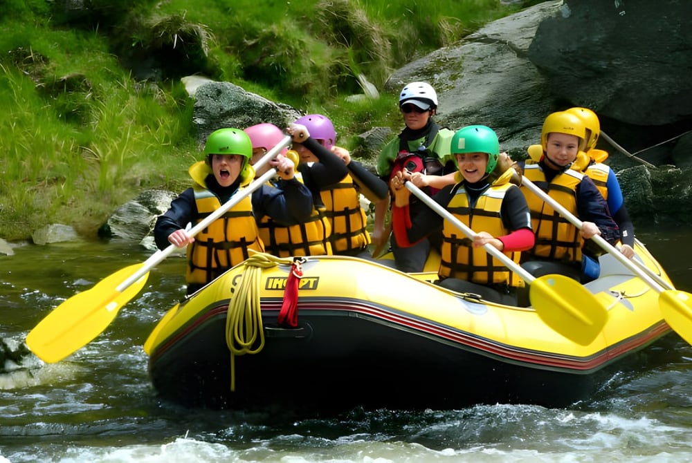 Schüler des Classic Plus Programms beim Befahren eines Flusses mit einem gelben Schlauchboot in grüner Umgebung.