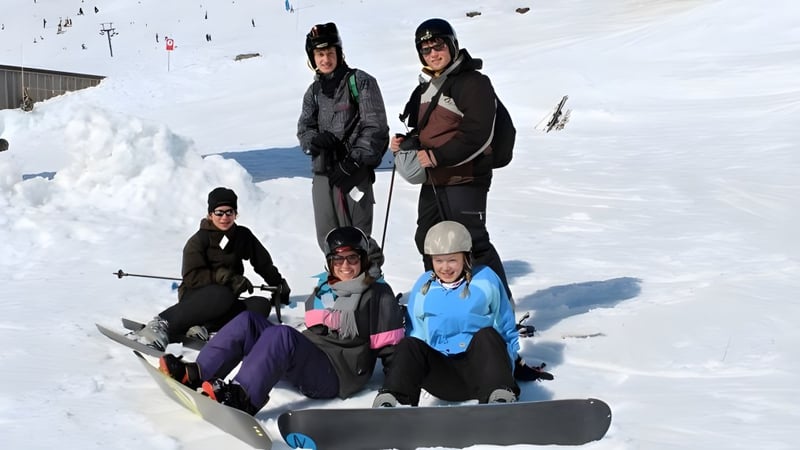 Schüler des Classic Plus Programms posieren gemeinsam in Skikleidung auf einem schneebedeckten Hang mit Skilift im Hintergrund.