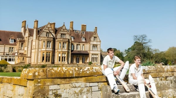 Zwei Menschen sitzen auf einer Steinmauer vor einem historischen Herrenhaus auf dem Gelände der Clayesmore School.