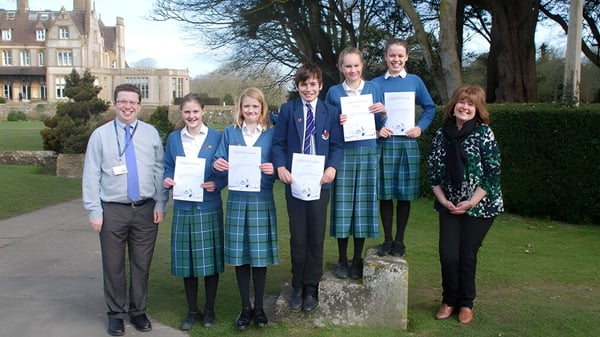 Schüler der Clayesmore School stehen mit Urkunden vor einem historischen Gebäude umgeben von Bäumen.