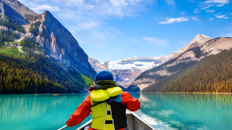Eine Person in bunter Outdoor-Ausrüstung steht in einem Boot auf dem See vor schneebedeckten Bergen bei der Clayton Heights Secondary School.