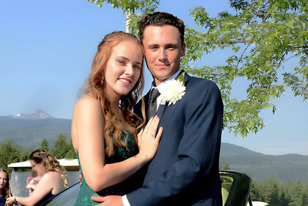 Ein Paar umarmt sich vor einer bergigen Landschaft auf dem Gelände der Clearwater Secondary School.