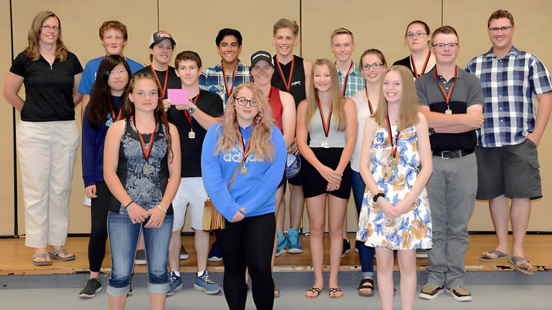 Eine Gruppe von Schülerinnen und Schülern mit Erwachsenen steht vor einer Holzvertäfelung in der Clearwater Secondary School.