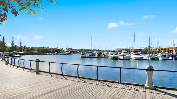 Ein Holzsteg führt an einer ruhigen Marina mit Segelbooten und Yachten auf dem Gelände der Cleveland District State High School vorbei.