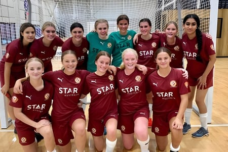 Die Fußballmannschaft der Cleveland District State High School posiert gemeinsam in der Sporthalle in roten und weißen Trikots mit STAR-Logo.