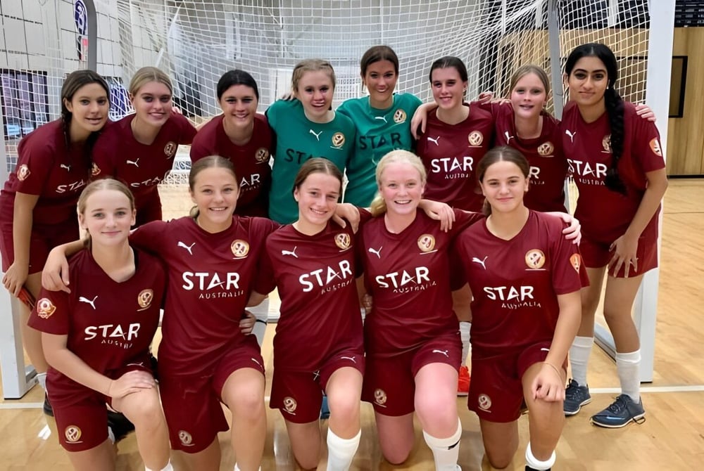 Die Fußballmannschaft der Cleveland District State High School posiert gemeinsam in der Sporthalle in roten und weißen Trikots mit STAR-Logo.