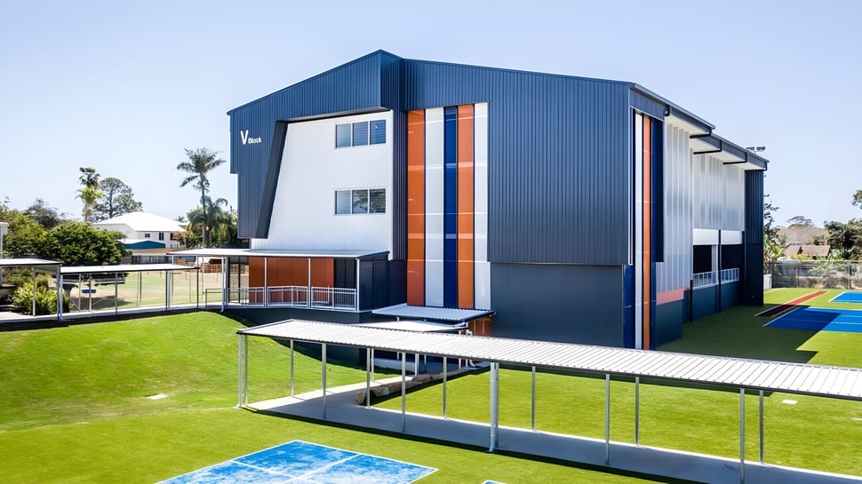 Das moderne mehrstöckige Gebäude der Cleveland District State High School mit blauer Fassade und orangen Akzenten steht auf einem Rasen mit Palmen.