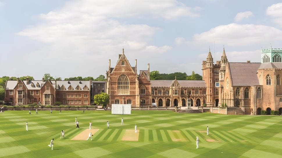 Schüler spielen Cricket auf dem Grün vor den historischen neugotischen Gebäuden des Clifton College.
