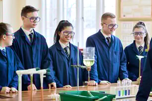 Schüler in akademischen Roben stehen im Labor des Clifton College um einen Tisch mit wissenschaftlicher Ausrüstung.