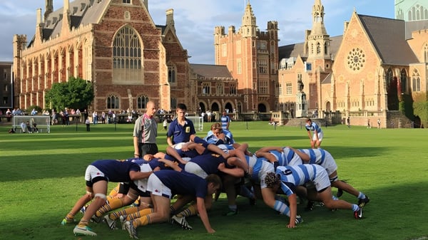 Eine Gruppe von Schülern in Sportkleidung bildet einen Kreis auf dem Sportplatz des Clifton College vor einem historischen Backsteingebäude.