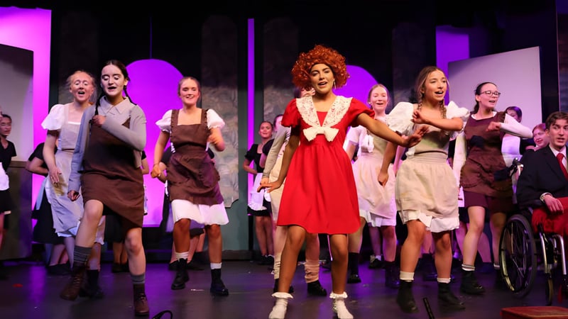 Auf der Bühne des Clonfert College treten mehrere Schülerinnen und Schüler bei einer Aufführung mit bunter Beleuchtung auf.